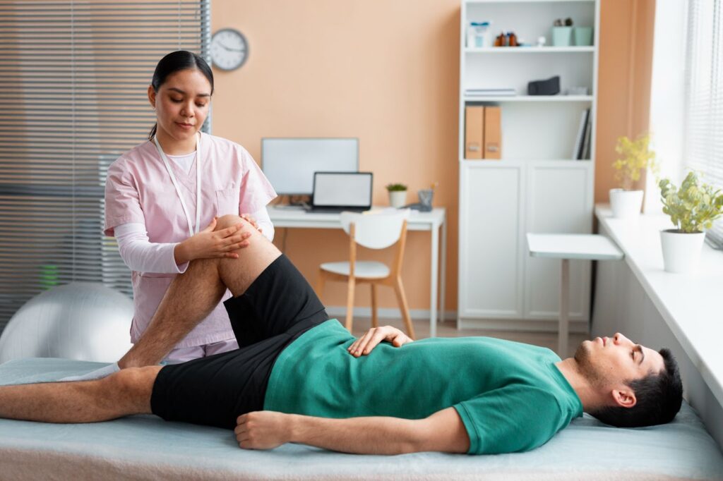 Physical therapist stretching a patient's leg on a mat in a bright clinic