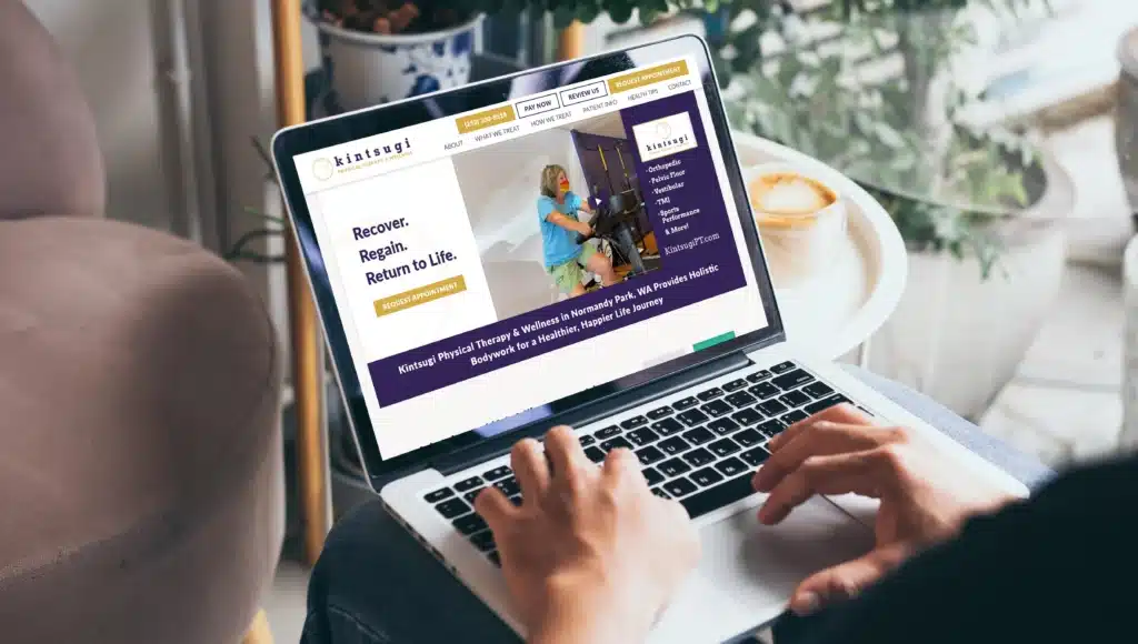 Person typing on a laptop displaying the Kintsugi Physical Therapy website homepage with the tagline "Recover. Regain. Return to Life."